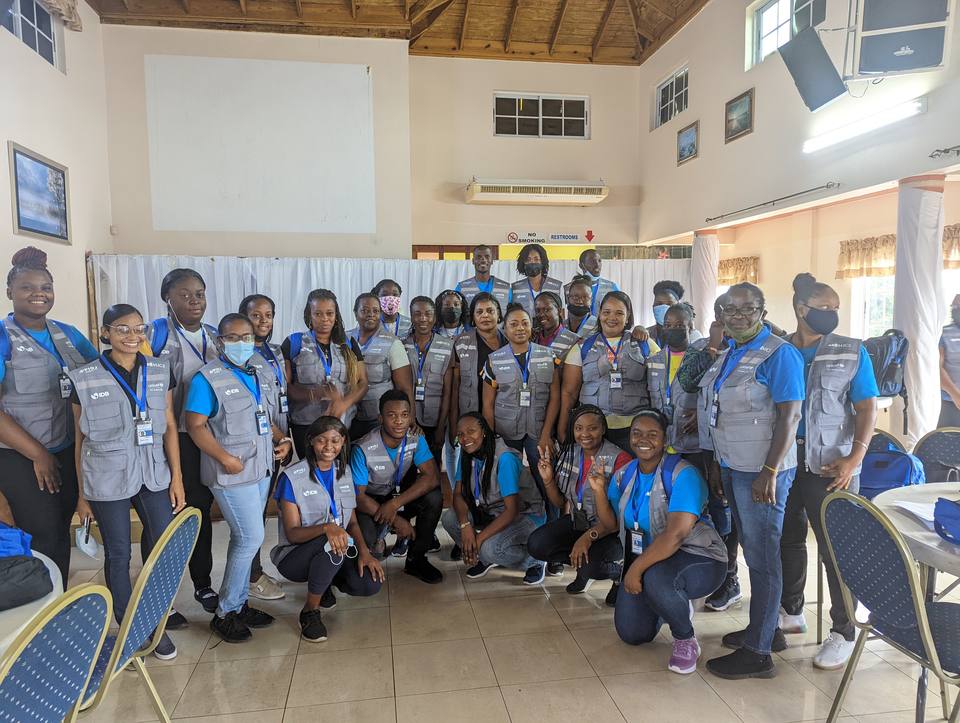 A cohort of MICS interviewers in field vests and shirts gathered in a training hall